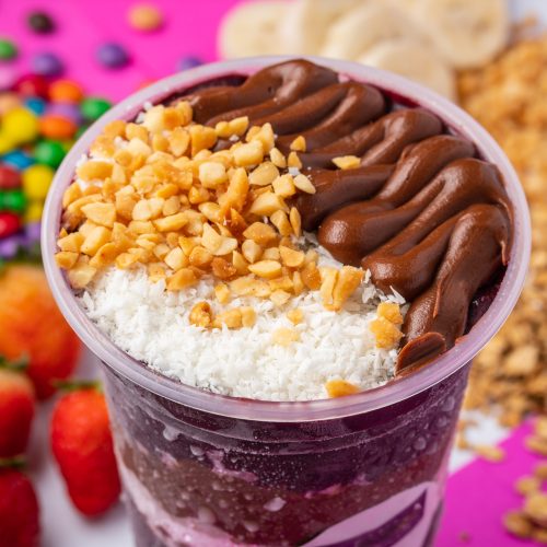 close up of acai or açaí cup with topping chocolate and nuts in colorful background